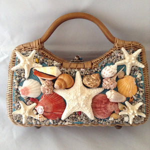 Lovely tan straw-grass purse made in Bali in the 1960s imagines a tropical sea bed with red silk lining. 1,014 shells, large and small, went into the making of this stunning piece. (Wanna count 'em?)  Dimensions - 8-1/2" Height; 13-1/2" Width"; 11 Length