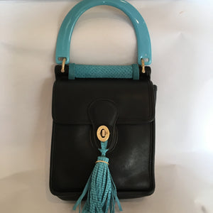 Formerly serious black Coach mailbag style purse becomes charming and witty with its exuberant teal handle and tassel. In the same contrasting color inside, the lining of genuine goat-skin is soft and supple as the gorgeous leather outside.