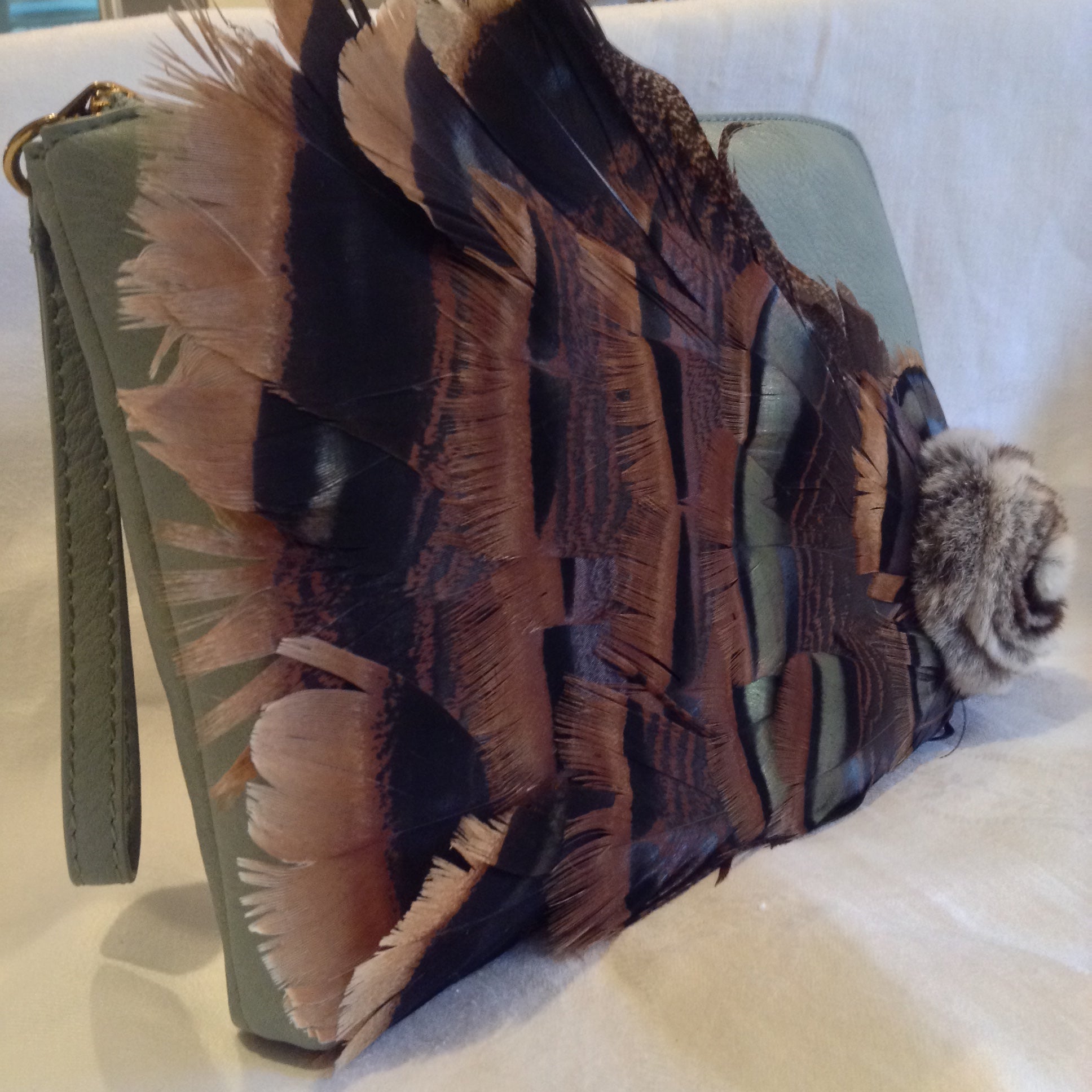 Iridescent turkey feathers and a mink pom-pom adorn this luscious teal vegan vintage leather clutch. With its inside zipper pocket & handy leather wrist strap it will even hold your notebook computer.  Dimensions - Height 9"; Width 11"; Depth 1" 