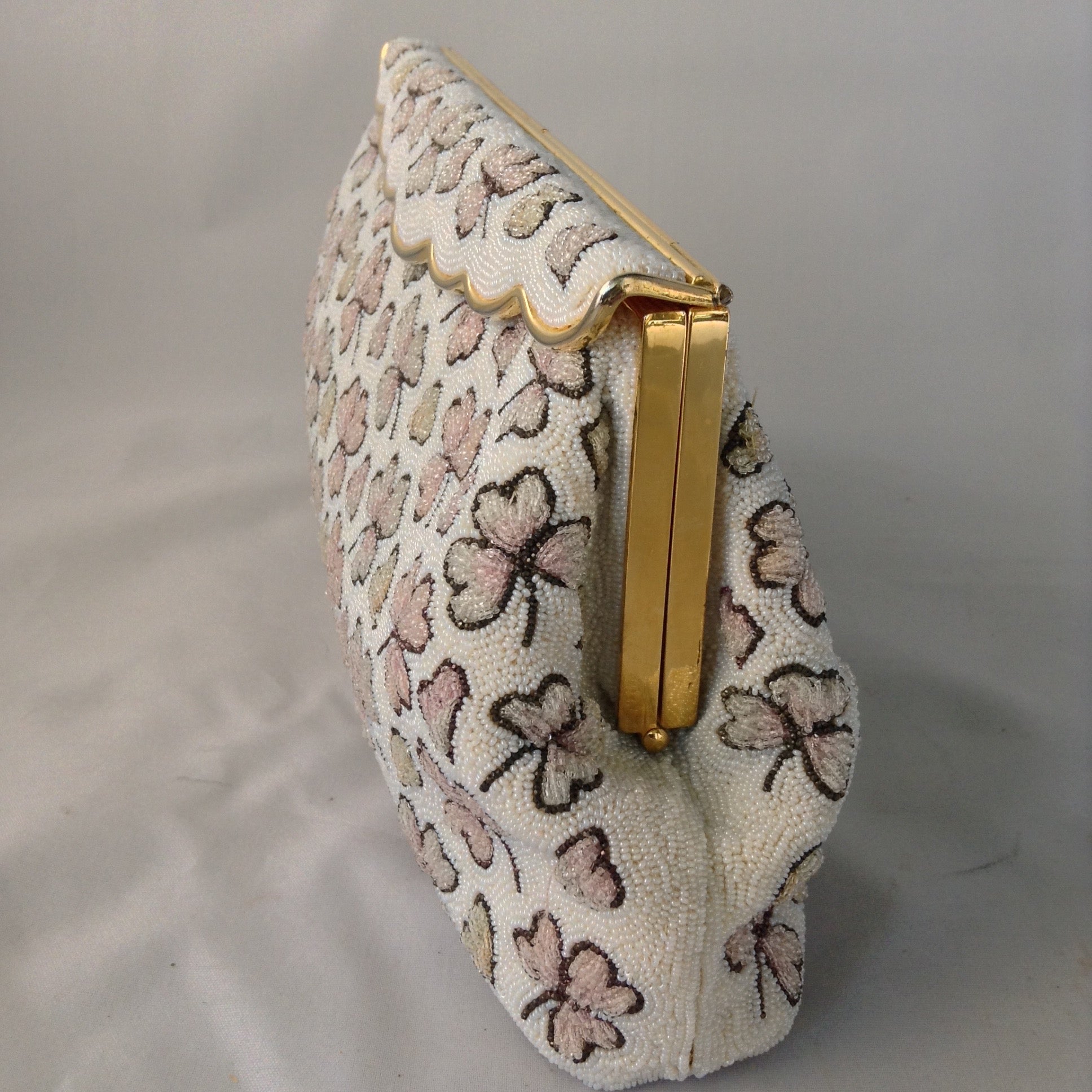 This vintage cream micro-beaded clover leaf clutch was made in France in the 1940s. It's covered with delicate light pink and green clovers and pink hearts too. Finally, it has a gold trim brass scalloped top that drapes over it's original vintage brass frame. They must not celebrate St. Patty in France because this gorgeous bag has never been used, but you'll carry it all Spring!  Dimensions - Height 5.5"; Length 9.5"; Depth 2"