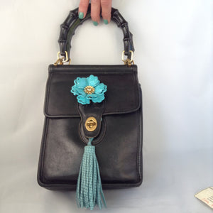 Formerly a staid and serious Coach mailbag, this supple black glove leather vintage purse becomes witty and charming with its enamel flower and new teal suede tassel and lining.  Dimensions - Height 9"; Width 7"; Depth 3"