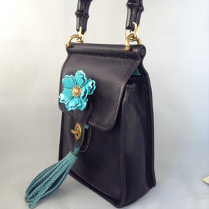 Formerly a staid and serious Coach mailbag, this supple black glove leather vintage purse becomes witty and charming with its enamel flower and new teal suede tassel and lining.  Dimensions - Height 9"; Width 7"; Depth 3"