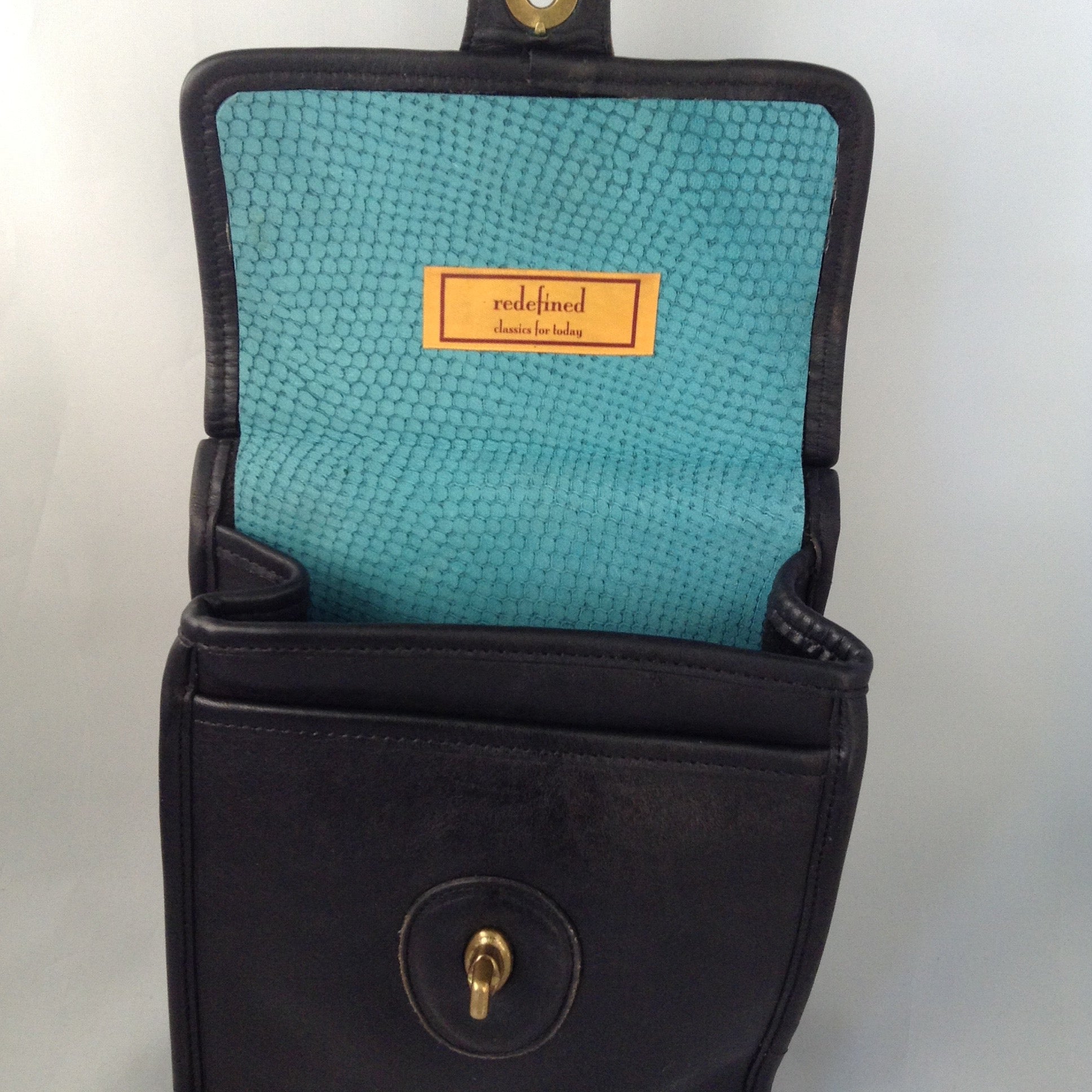Formerly a staid and serious Coach mailbag, this supple black glove leather vintage purse becomes witty and charming with its enamel flower and new teal suede tassel and lining.  Dimensions - Height 9"; Width 7"; Depth 3"