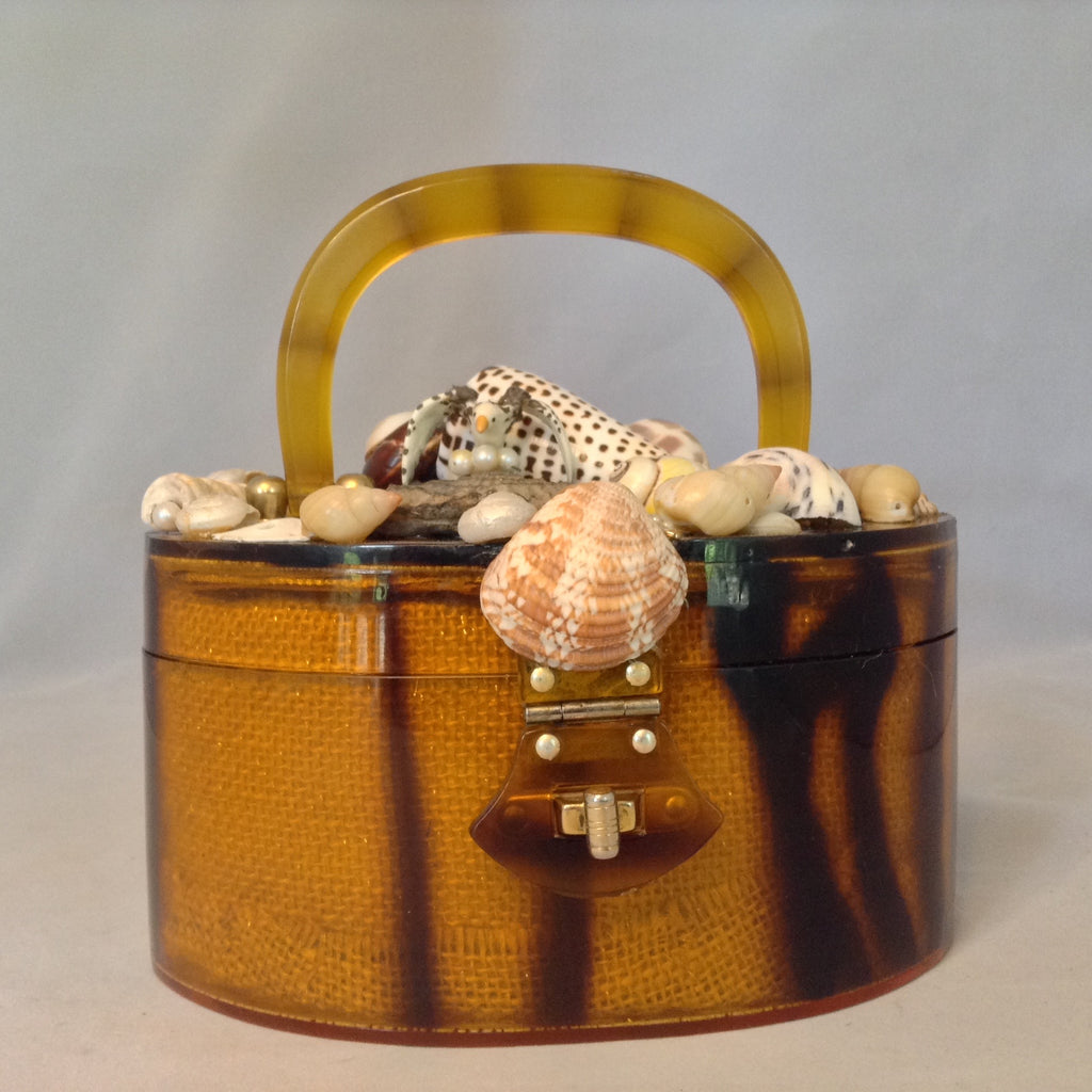 Vintage Amber Lucite Oval Purse Topped With Multi-Colored Seashells And A Tiny Pelican Guarding Her Eggs. Mirror On Inside Top. Original Golden Brass Hardware. Dimensions - Height 3.75"; Width 7.5"; Depth 3.75"; Handle 3.25"