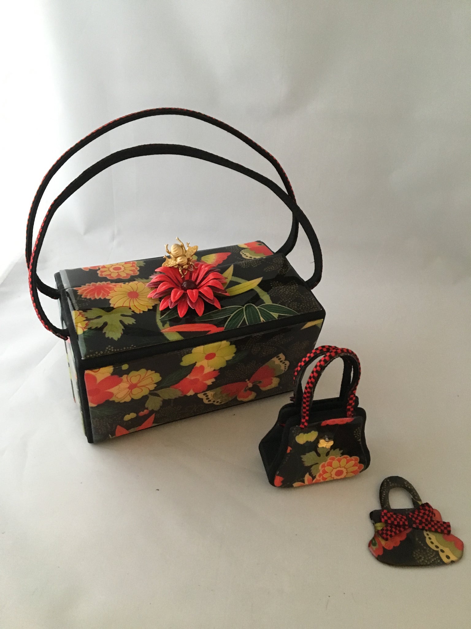 Vintage box purse with flowers and butterflies. From its cheeky checkerboard handle to its vintage enamel daisy with bouncy pouncy bee, this brilliant handbag will take you from spring through fall. Included are a matching purse for your little girl and her dolly, too!  Dimensions - Height 4.5"; Width 7"; Depth 4.5"; Handle 6"